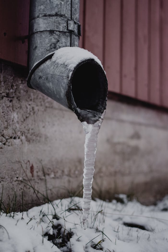 Frozen drain spout with icicle against a snowy backdrop. Captured in Estonia.